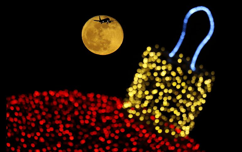 La Luna brilla detrás de decoraciones navideñas mientras un avión se prepara para aterrizar en el aeropuerto de Larnaca, en Chipre. AFP/P. Karadjias