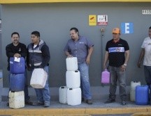 Ciudadanos esperan en una estación de servicio a surtir gasolina en recipientes de plástico; uno de ellos carga con un envase de detergente. EL INFORMADOR / F. Atilano