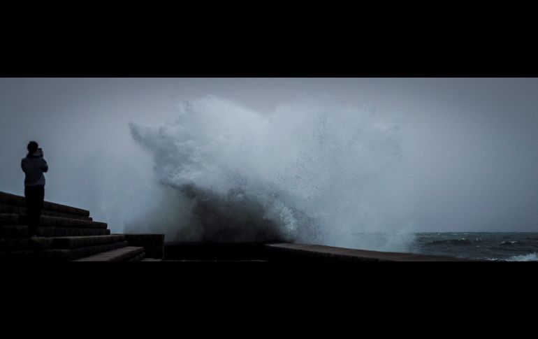 Una mujer observa cómo saltan las olas en el paseo de Chillida de la ciudad española de San Sebastián,  donde este viernes los cielos se presentan nubosos o cubiertos con brumas y bancos de niebla. EFE/J. Etxezarreta