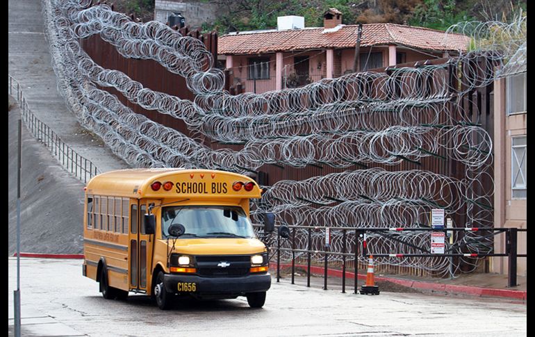 Un autobús escolar pasa junto a la barda reforzada con alambre de púas en el centro de Nogales, Arizona.