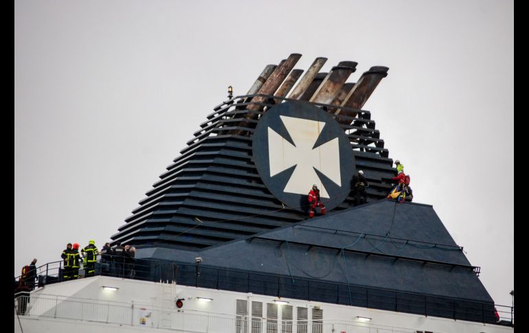 Bomberos intentan que migrantes bajen de la chimenea de un barco en el puerto francés de Calais, luego de que los migrantes rompieron el perímetro del puerto y subieron, en su intento por llegar a Inglaterra. AFP/B. Barron
