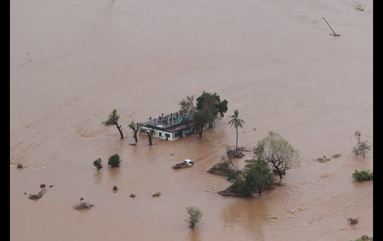 Personas se ven el techo de una casa inundada.