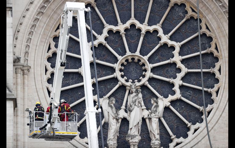 Varios bomberos trabajan en un elevador junto a la fachada de catedral.