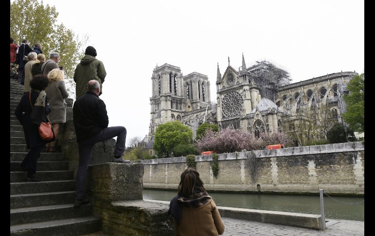 El incendio destruyó su aguja y parte de su techo, pero que no afectó a sus campanarios ni a la llamada Corona de Cristo. Personas observan la catedral a orillas del río Sena. AFP/B. Guay