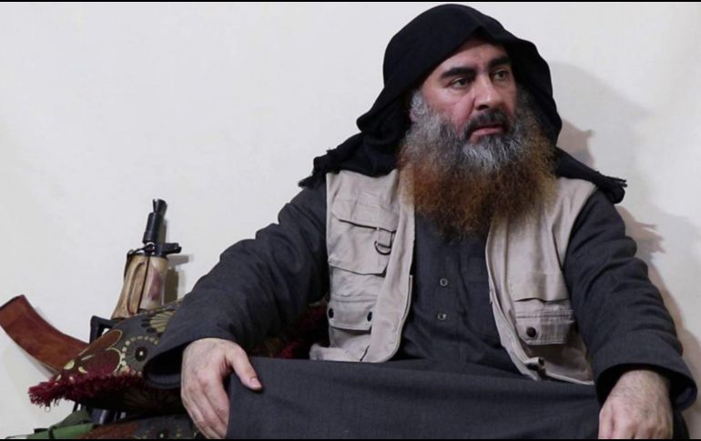 Abu Bakr al Bagdadi aparece sentado en el suelo, sobre unos cojines y con las piernas cruzadas; a su lado se puede ver un rifle apoyado en una pared. TWITTER/@laleyro