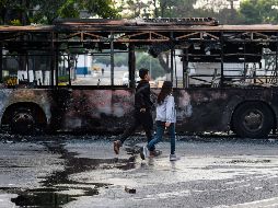 Personas pasan  junto a un autobús calcinado, luego de los enfrentamientos de ayer en Caracas. AFP/M. Delacroix