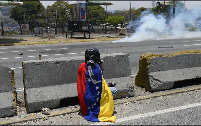 Un manifestante se resguarda de gases lacrimógenos en las cercanías de la base militar La Carlota en Caracas. AFP/M. Delacroix