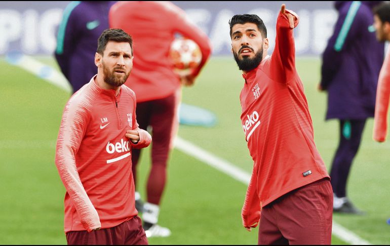Lio y Luis Suárez dialogan en la grama de Anfield, donde hoy van por el ansiado pase al partido por el título. EFE