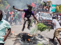 Un hombre salta por encima de un neumático en llamas, este domingo, durante una manifestación para exigir la dimisión del presidente haitiano, en Puerto Príncipe. EFE/J. Herve