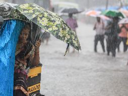 Una mujer india se protege con un paraguas mientras atraviesa en mototaxi una calle inundada a causa de las lluvias monzónicas. EFE/D. Solanki