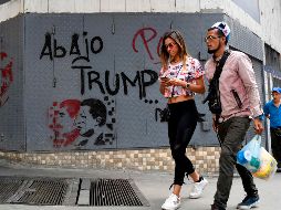 Personas caminan frente a un muro que tiene la inscripción: 