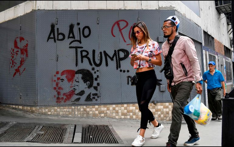 Personas caminan frente a un muro que tiene la inscripción: 