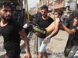 Jóvenes cargan a un manifestante herido durante enfrentamientos con policías en Bagdad. AFP/A. Al-Rubaye