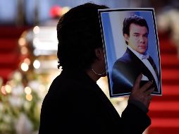 Una persona sostiene una imagen de José José mientras pasa por enfrente del ataúd que resguarda la mitad de las cenizas del artista mexicano. AFP / A. Estrella