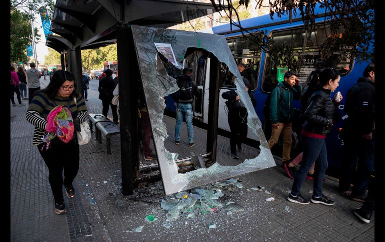 Habitantes aguardan para tomar un autobús en una parada vandalizada. AFP/P. Ugarte