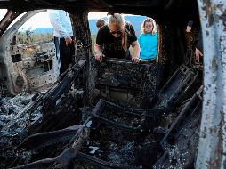 Miembros de la familia LeBarón miran el automóvil calcinado luego del ataque en el que murieron nueve de sus integrantes. AFP / H. Martínez