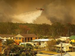 Un helicóptero del Servicio Rural de Bomberos descarga agua sobre los incendios que arrasan este viernes los bosques de la ciudad de Harrington. EFE/S. Chalker