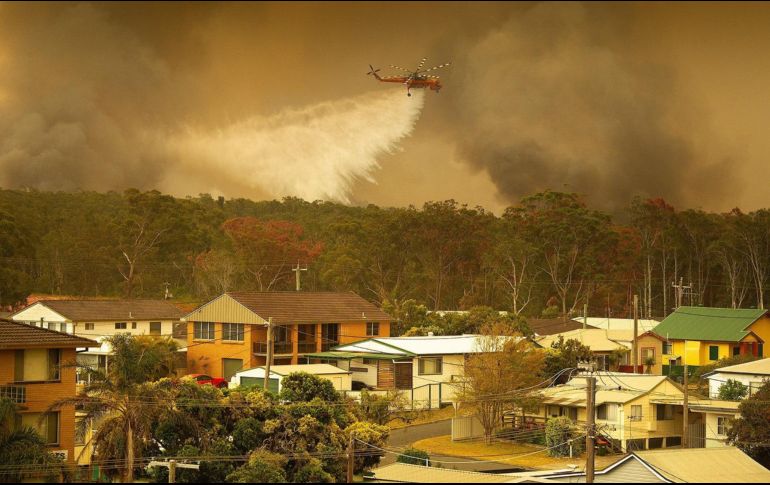 Un helicóptero del Servicio Rural de Bomberos descarga agua sobre los incendios que arrasan este viernes los bosques de la ciudad de Harrington. EFE/S. Chalker