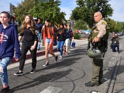 Policías vigilan a estudiantes que hacen fila para ingresar a autobuses que los trasladarán a lugares seguros. AFP/F. Brown