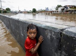 Un niño se protege tras un muro en una carretera inundada de Yakarta. EFE/M. Irham