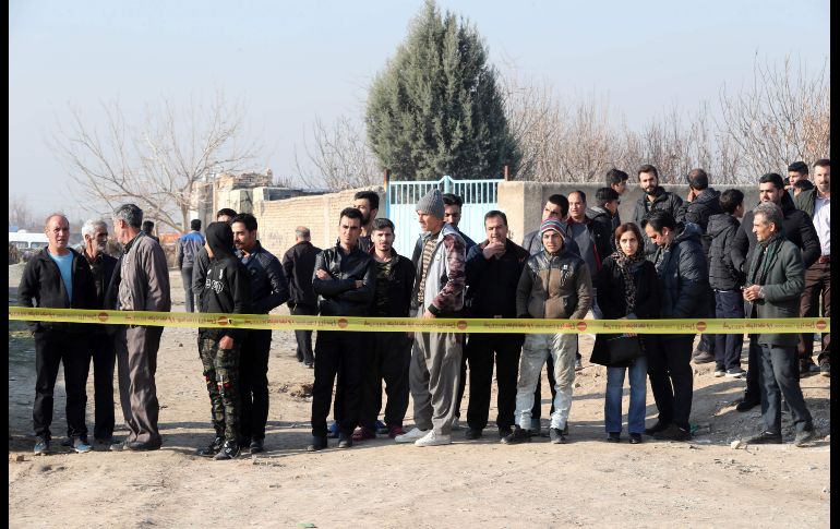 Personas observan el sitio del accidente tras un cordón de seguridad. AFP