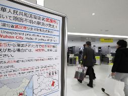 Pasajeros pasan junto a un letrero de advertencia sanitaria en el aeropuerto de Narita, en la prefectura de Chiba. AFP/JIJI PRESS