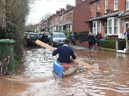 Un hombre usa una tabla de madera para remar un kayak para transportarse en medio de una calle inundada en Ross-on-Wye, al oeste de Inglaterra. AFP/O. Scarff