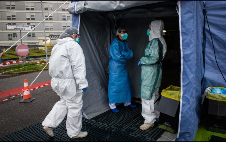 Trabajadores de la salud que usan trajes y máscaras protectoras entran a una unidad médica avanzada, construida frente al Hospital Cremona, en Italia. EFE/M. Corner