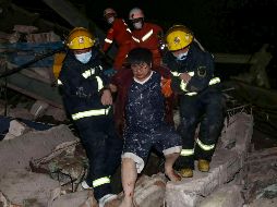 Trabajadores de rescate, vestidos con overoles anaranjados, trepan sobre escombros y estructuras metálicas retorcidas del hotel para sacar a las víctimas. AFP