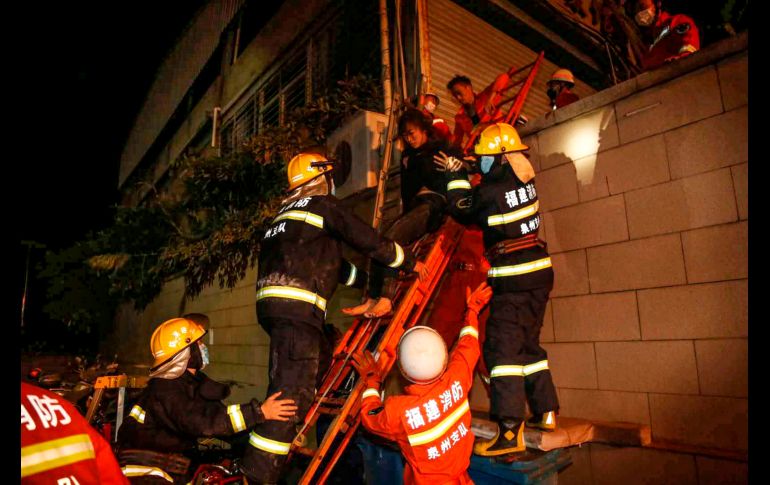 Trabajadores de rescate, vestidos con overoles anaranjados, trepan sobre escombros y estructuras metálicas retorcidas del hotel para sacar a las víctimas. AFP