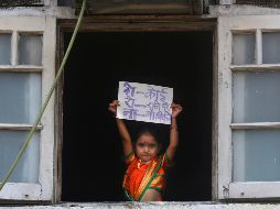 Una niña en atuendo tradicional para una celebración en la India muestra desde una ventana un letrero que dice 