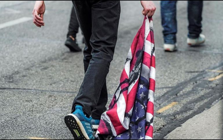 Un manifestante arrastra una bandera de los Estados Unidos durante una protesta después de la visita del presidente Donald Trump en Kenosha. EFE/T. Maury