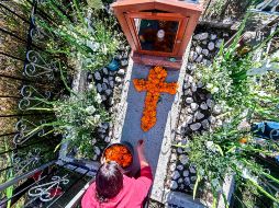Una mujer decora este domingo la tumba de un familiar en el panteón Magdalena en  San Pedro Cholula, Puebla. Autoridades locales restringieron los horarios y el números de visitantes a los cementerios. AFP/P. Pardo
