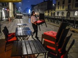 Una empleada de un restaurante recoge sillas y mesas previo a la hora del cierre, en Milan. EFE/M. Corner