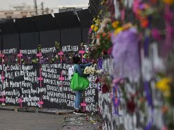 Una mujer coloca flores en las vallas metálicas afuera de Palacio Nacional junto a los nombres de víctimas de feminicidios. EFE / S. Gutiérrez