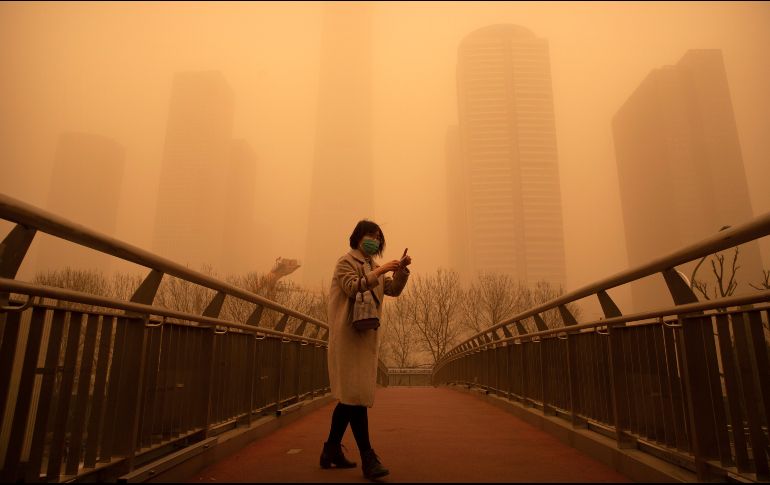 Una mujer camina por un puente peatonal durante la tormenta de arena en Pekín, China. AP/M. Schiefelbein