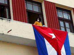 Una mujer sale al balcón donde se expone una bandera cubana, este martes en La Habana. EFE/E. Mastrascusa