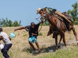 Medios estadounidenses retomaron esta imagen de un agente de la Patrulla Fronteriza de EU  que intenta impedir que un haitiano ingrese al campamento cerca del puente internacional de Del Río, Texas. AFP/P. Ratje
