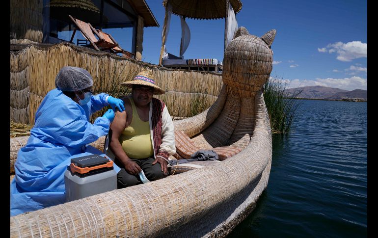 La obstetra Deysi Barriga anuncia la llegada del bote a las islas, mientras que el técnico Sebastián Quispe dirige la pequeña nave que transporta un recipiente con vacunas de Pfizer. AP/M. Mejía.jpg-15cec.jpg