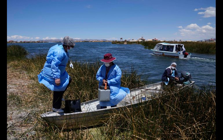 La obstetra Deysi Barriga anuncia la llegada del bote a las islas, mientras que el técnico Sebastián Quispe dirige la pequeña nave que transporta un recipiente con vacunas de Pfizer. AP/M. Mejía