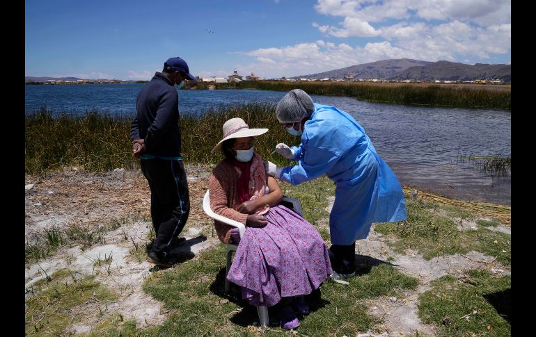 La obstetra Deysi Barriga anuncia la llegada del bote a las islas, mientras que el técnico Sebastián Quispe dirige la pequeña nave que transporta un recipiente con vacunas de Pfizer. AP/M. Mejía