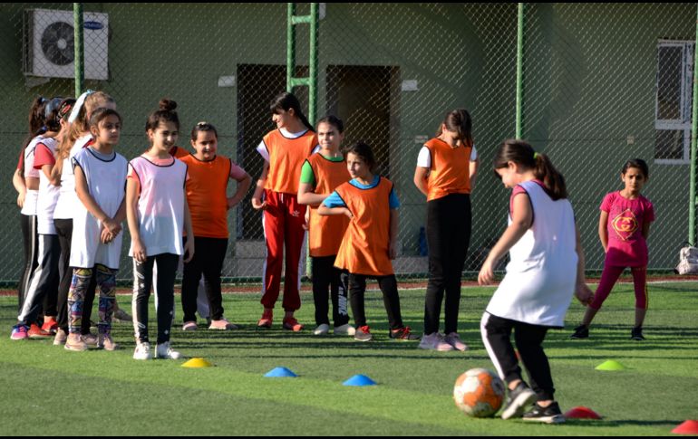 Usando petos coloridos, las niñas hacen ejercicios de estiramiento en el césped antes de que Yusef Chaba sople el silbato para comenzar la práctica. AFP/Z. Al Obeidi