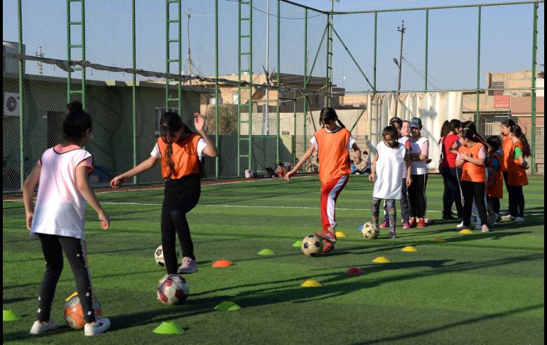 Usando petos coloridos, las niñas hacen ejercicios de estiramiento en el césped antes de que Yusef Chaba sople el silbato para comenzar la práctica. AFP/Z. Al Obeidi