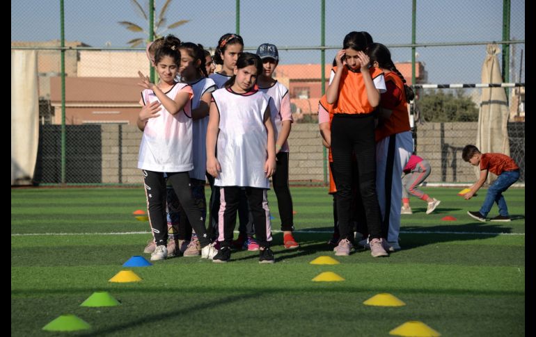 Usando petos coloridos, las niñas hacen ejercicios de estiramiento en el césped antes de que Yusef Chaba sople el silbato para comenzar la práctica. AFP/Z. Al Obeidi