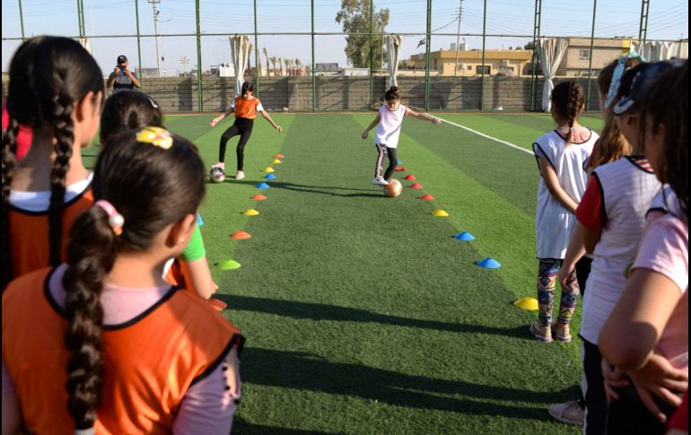 Usando petos coloridos, las niñas hacen ejercicios de estiramiento en el césped antes de que Yusef Chaba sople el silbato para comenzar la práctica. AFP/Z. Al Obeidi