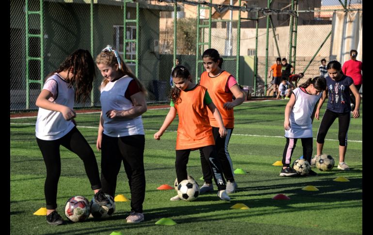 Usando petos coloridos, las niñas hacen ejercicios de estiramiento en el césped antes de que Yusef Chaba sople el silbato para comenzar la práctica. AFP/Z. Al Obeidi