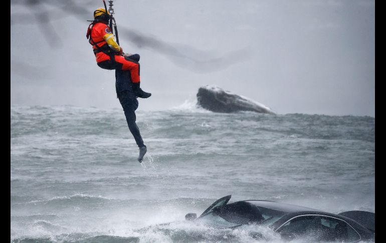 Un guardacosta colgado de un cable de un helicóptero se posicionó encima del vehículo, en medio de una ventisca. AP/J. Barnes