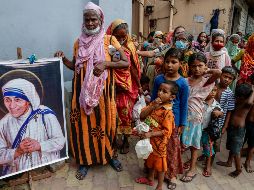 Personas sin hogar al lado de un cuadro de santa Teresa de Calculta afuera de la sede de las Misioneras de la caridad. AP/B. Das
