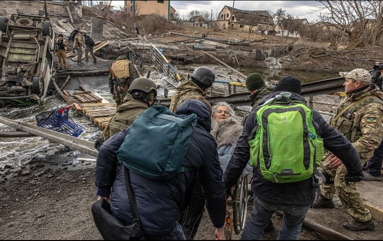 Soldados ucranianos y civiles cargan a una mujer de la tercera edad en un campo destruido por los enfrentamientos con Rusia. EF E/ R. Pilipey