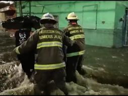 Personal de Proteccion Civil asiste a ciudadanos en medio de la corriente de agua que se formó en las calles Manuel Doblado e Industria, en La Perla. TWITTER/PCJalisco